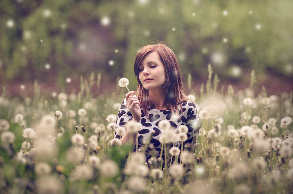 Serene woman with dandelion in blooming field, surrounded by nature's tranquility.