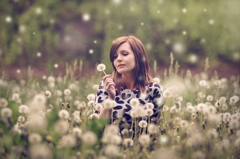 Serene woman with dandelion in blooming field, surrounded by nature's tranquility.